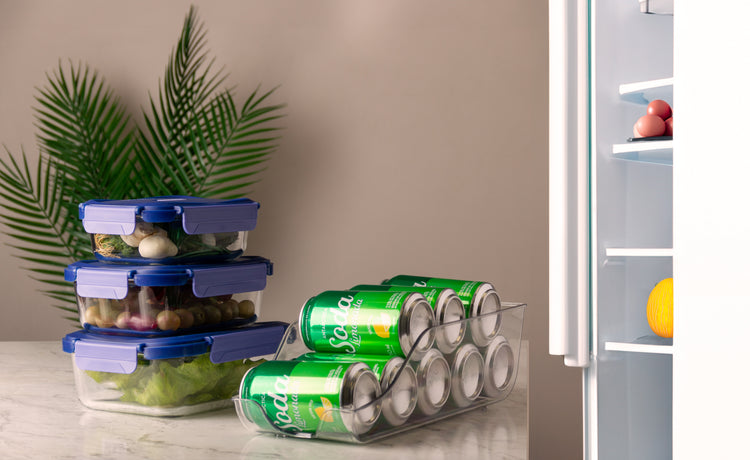 Organizadores de geladeira com potes herméticos empilhados e suporte acrílico para latas ao lado de geladeira aberta.